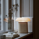 Nova Table Lamp by Woud in ivory travertine with opal glass shade on a window sill.